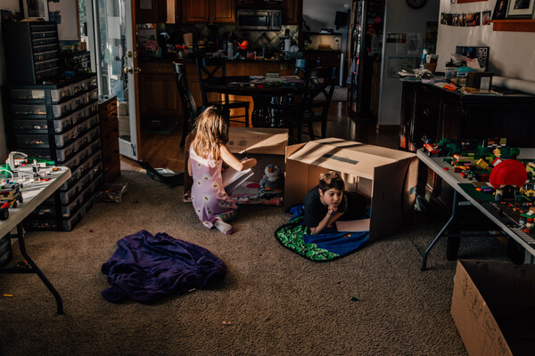 Two kids sitting amongst their toys inside cardboard boxes